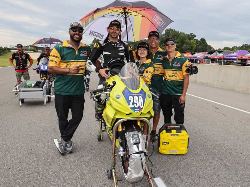 A group of people next to a motorcycle racers on the grid.