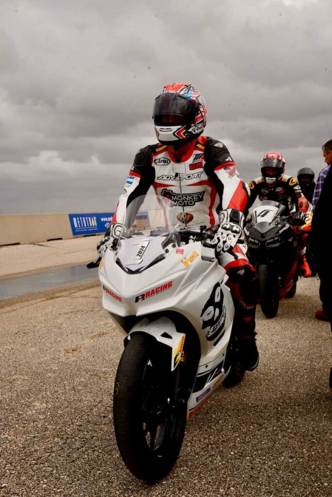 a motorcycle racer in leathers and helmet with clouds in the background on track