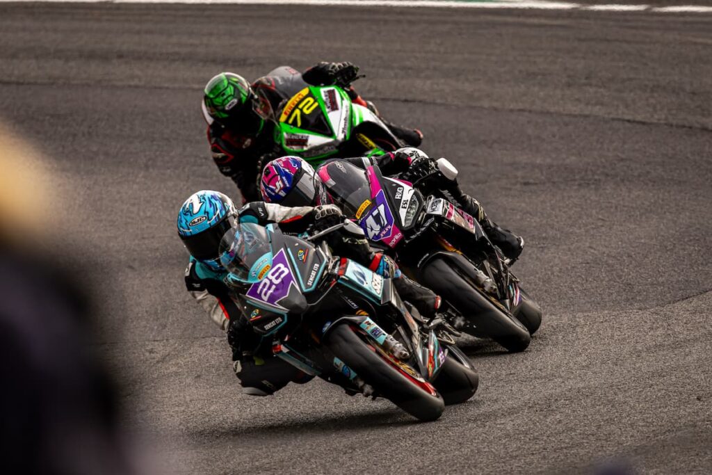 a group of motorcycle racers chasing each other leaned at the apex