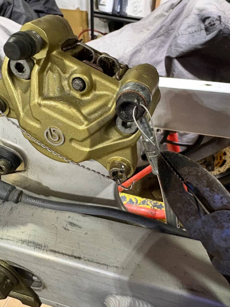 Motorcycle brake caliper is being safety wired by plier