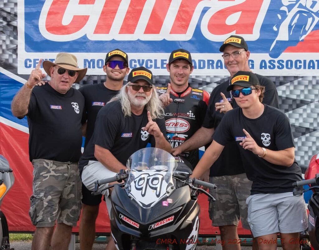 a group of people in the paddock celebrating the win, showing number one with their finger