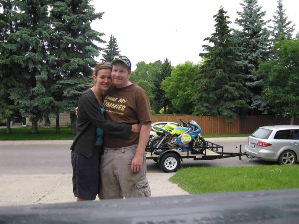 a couple hugging each other with their motorcycle on the trailer in the background